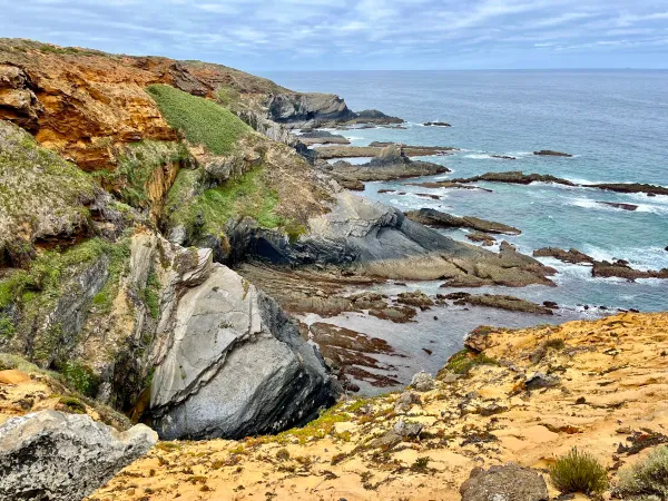 Scenic view of rugged cliffs and the Atlantic coastline along the Fishermen's Trail in Portugal, with green vegetation and rocky formations visible.